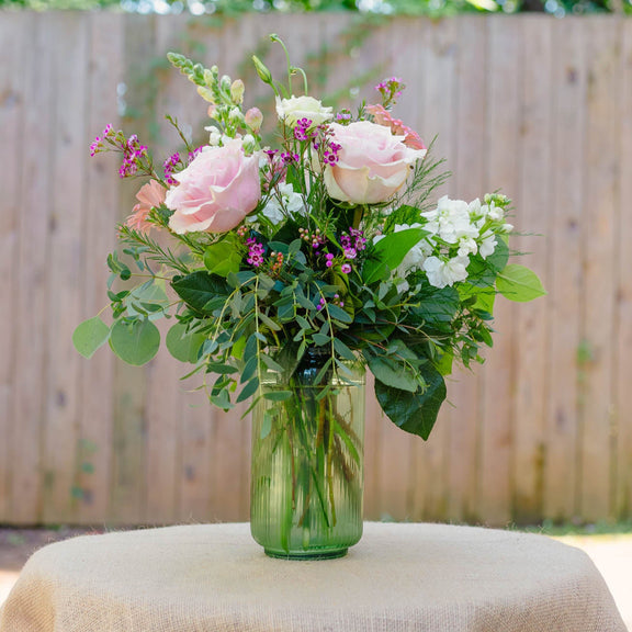 Bouquet of flowers in a clear vase on a table outdoors.