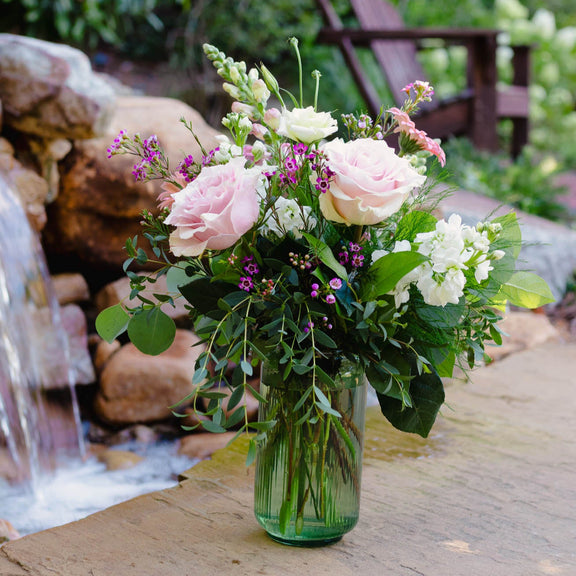 Bouquet of flowers in a clear vase on a wooden surface with a natural background
