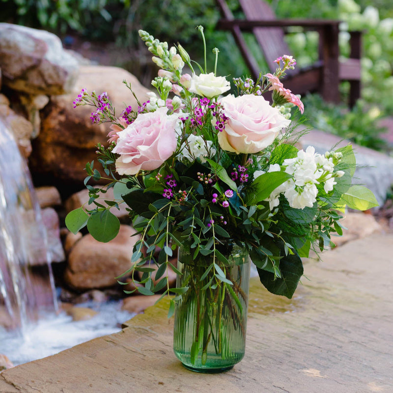 Bouquet of flowers in a clear vase on a wooden surface with a natural background