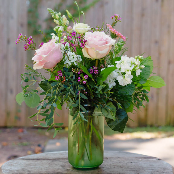 Bouquet of flowers in a green vase on a wooden table with a blurred natural background