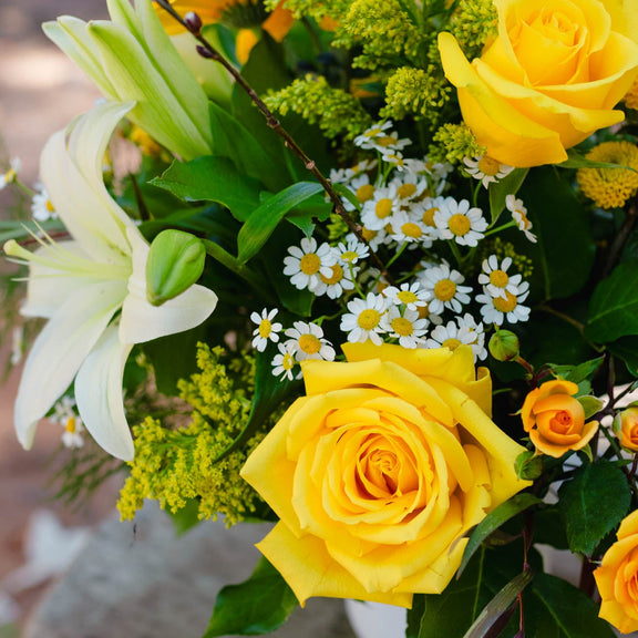 Bouquet of yellow roses and white lilies with greenery on a textured surface.