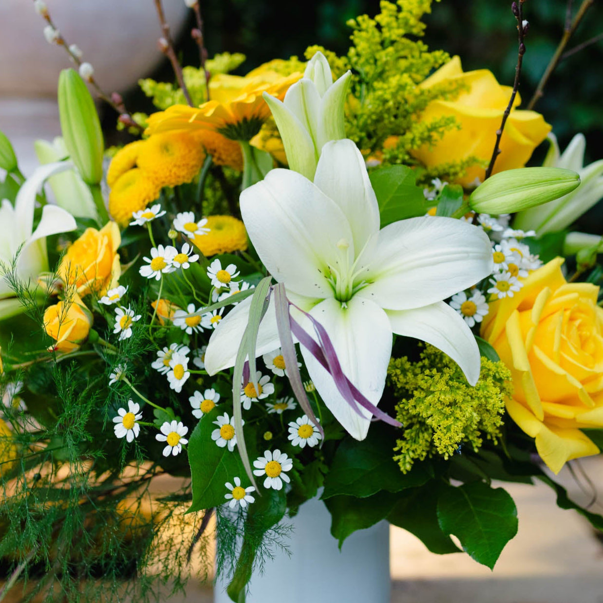 Bouquet of white lilies, yellow roses, and greenery in a vase.