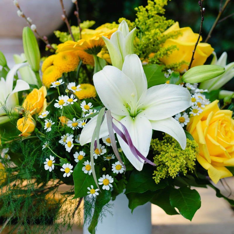 Bouquet of white lilies, yellow roses, and greenery in a vase.