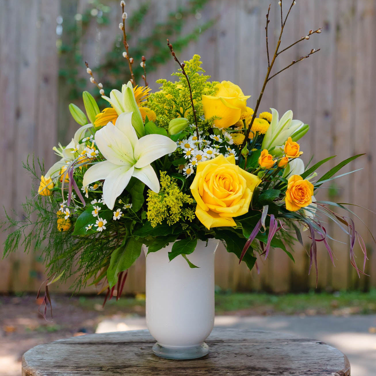 Floral arrangement with yellow and white flowers in a white vase on a wooden surface.