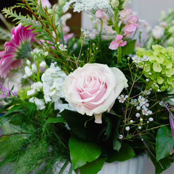 Bouquet of flowers with pink roses and greenery in a white vase.