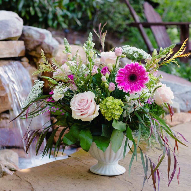 Floral arrangement in a white vase on a stone surface with a garden background