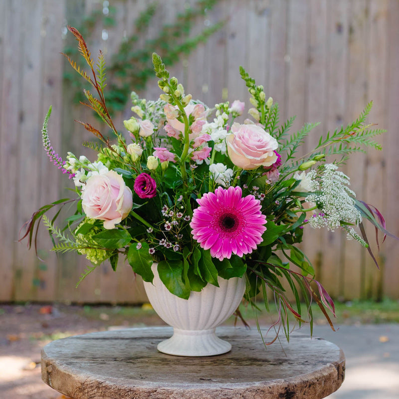 Floral arrangement in a white vase on a wooden table with a blurred green and brown background