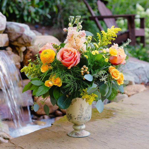 Floral arrangement in a decorative vase on a stone surface with a water feature in the background