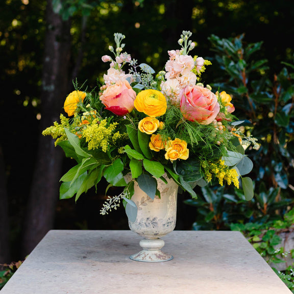Floral arrangement in a vase on a stone pedestal with greenery in the background
