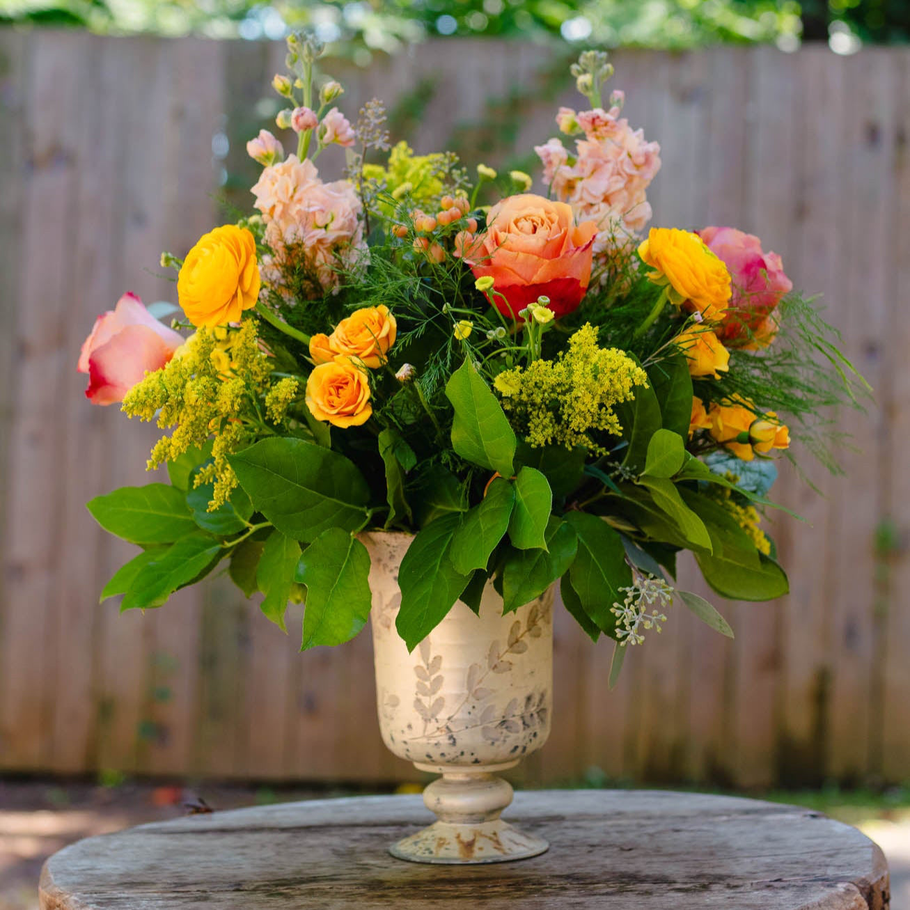 Floral arrangement in a decorative vase on a wooden table with a blurred green background