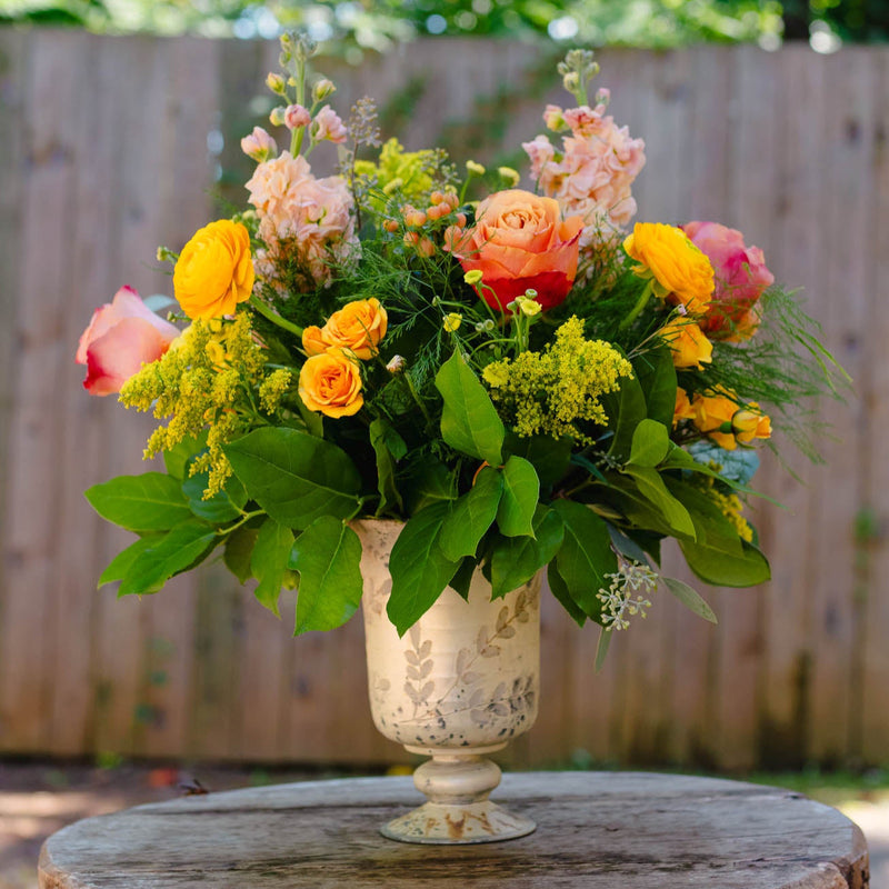 Floral arrangement in a decorative vase on a wooden table with a blurred green background