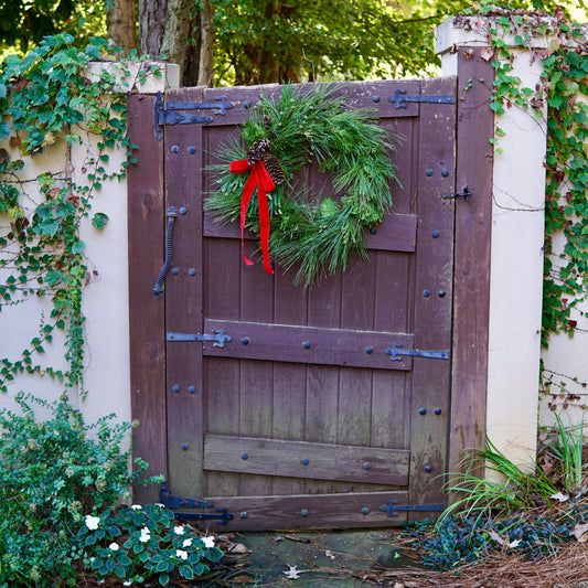 Wooden gate with a wreath and red ribbon in a garden setting