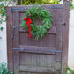 Wooden gate with a green wreath and red ribbon, surrounded by greenery.