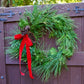 Green wreath with red ribbon and pinecones on a wooden door outdoors
