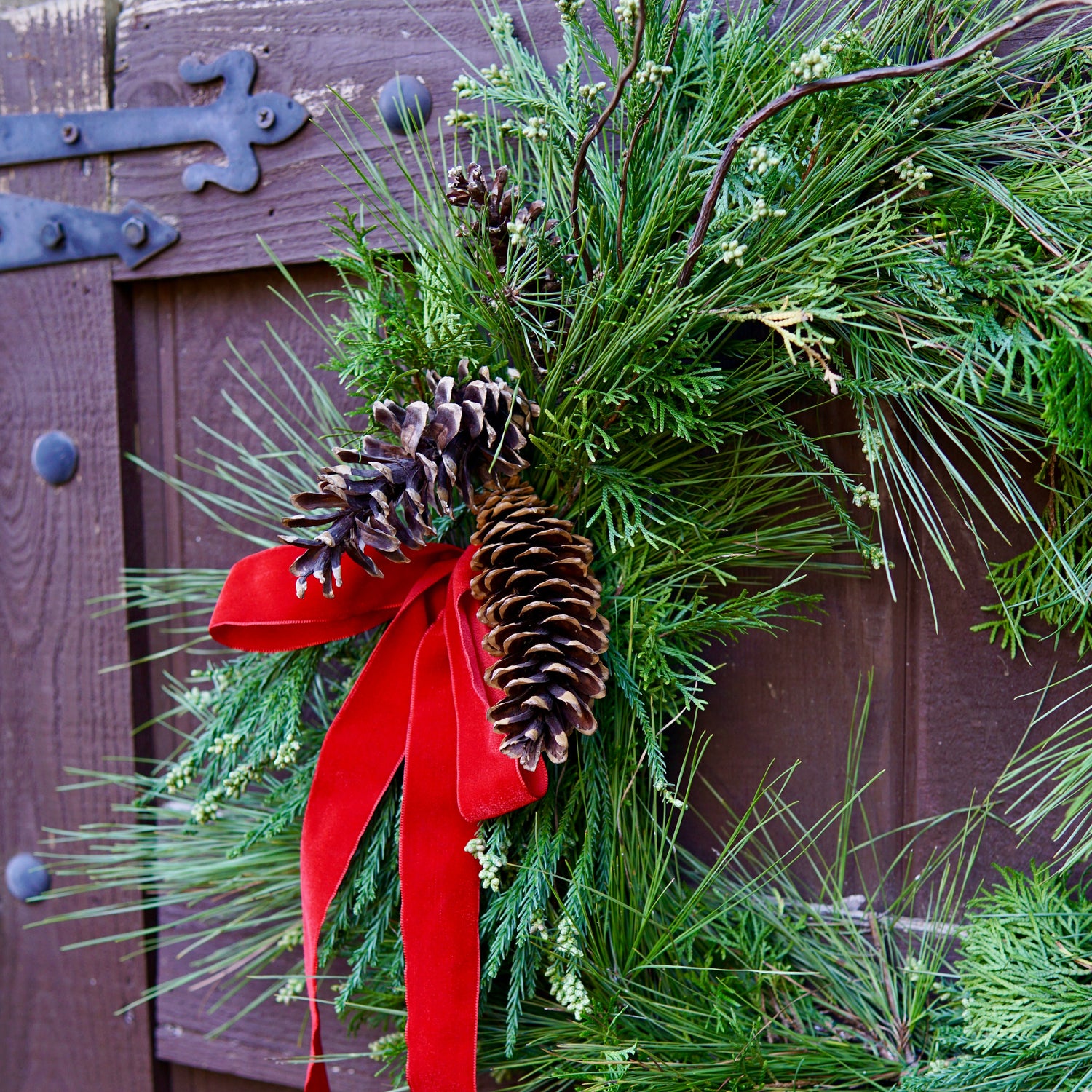 Green wreath with pine cones and a red ribbon on a wooden door