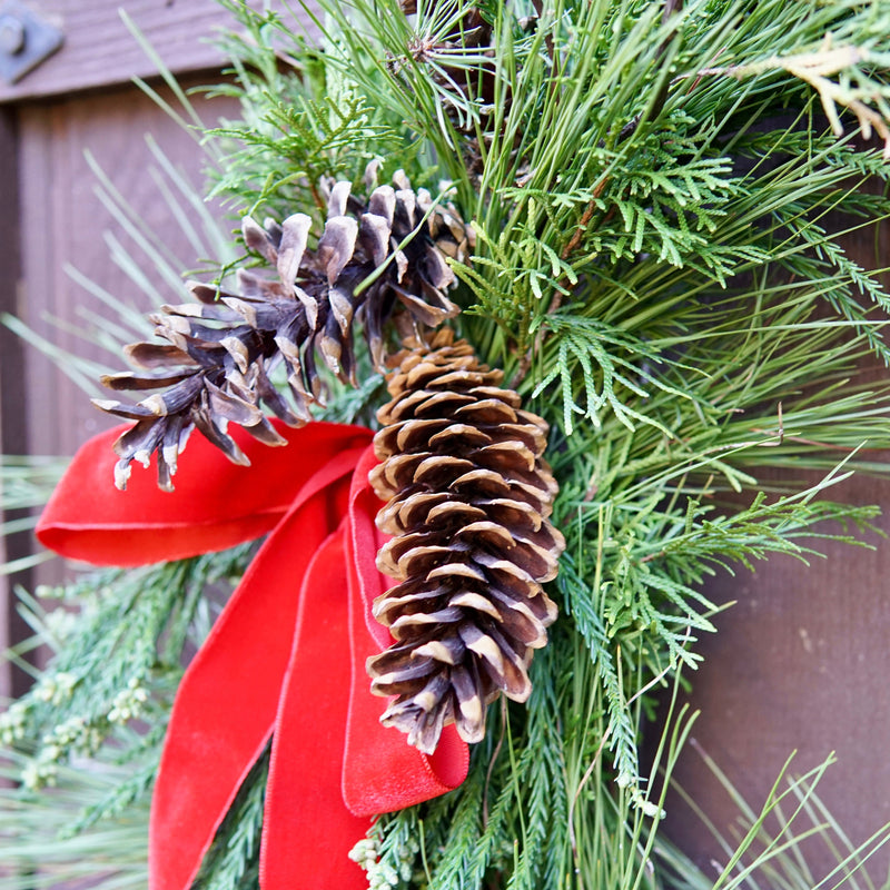 Decorative wreath with pine cones and a red ribbon against a wooden background