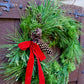 Green wreath with red ribbon and pinecones on a wooden door