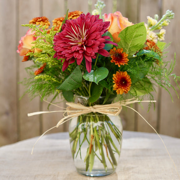 Bouquet of flowers in a clear vase with a natural bow on a wooden surface