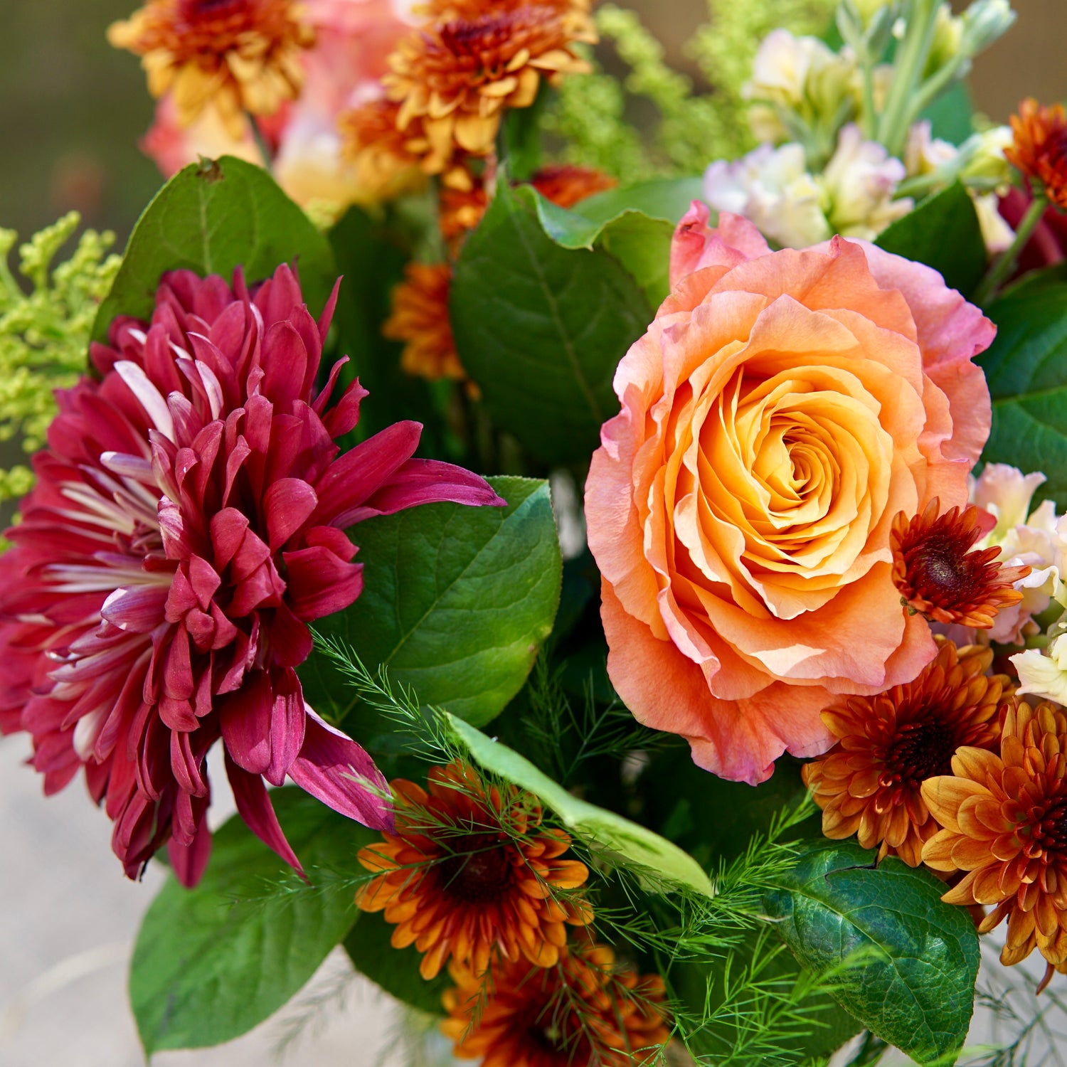Bouquet of flowers with a pink rose and maroon flower.