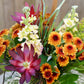 Bouquet of colorful flowers including purple, yellow, and orange with green leaves.