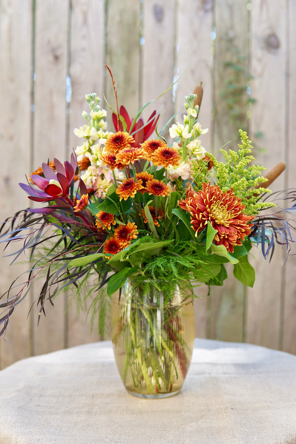 Bouquet of flowers in a clear vase on a white surface with a wooden background