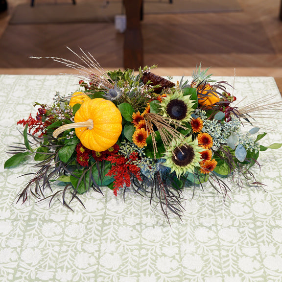 Decorative floral arrangement with pumpkins and sunflowers on a patterned tablecloth.