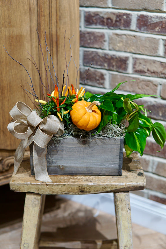 Decorative arrangement with pumpkins and greenery on a wooden stool against a brick wall.