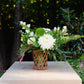 Floral arrangement in a woven basket on a stone pedestal with a blurred green background