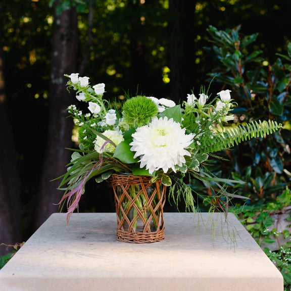 Floral arrangement in a woven basket on a stone pedestal with a blurred green background