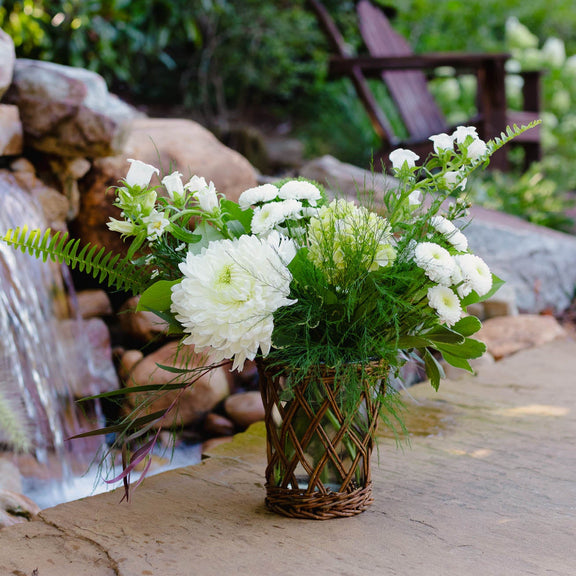Bouquet of white flowers in a woven basket on a stone surface with a natural background