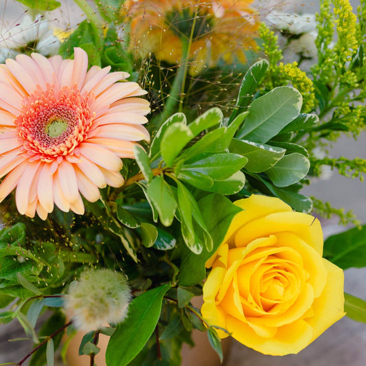 Bouquet of flowers including a yellow rose and peach-colored daisy in a vase.