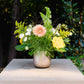 Floral arrangement in a vase on a stone ledge with greenery in the background