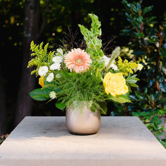 Floral arrangement in a vase on a stone ledge with greenery in the background