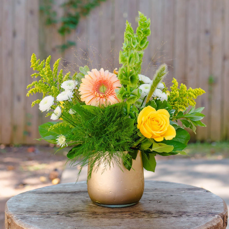 Floral arrangement in a gold vase on a wooden table with a blurred background