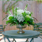 Floral arrangement on a round table with green chairs in a garden setting