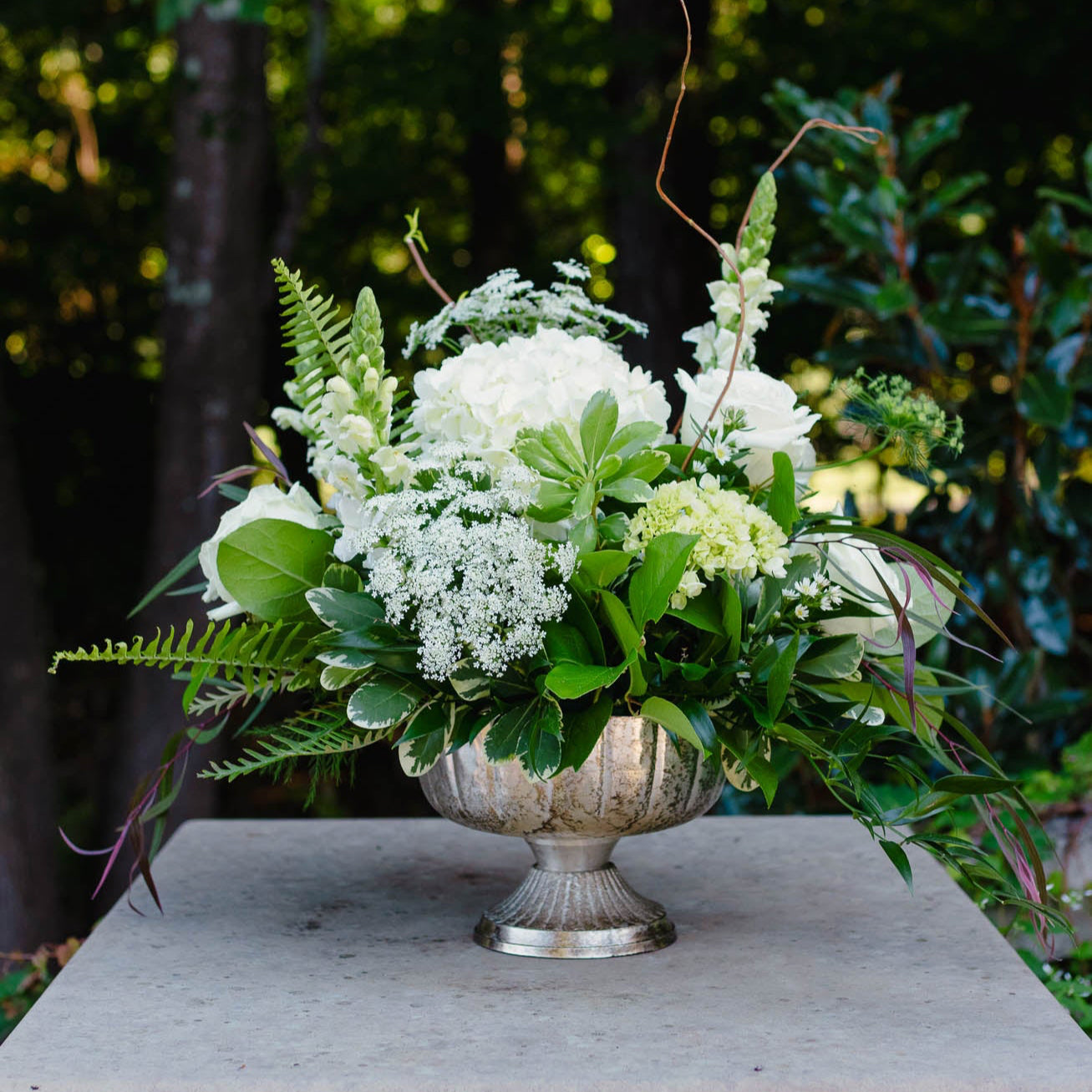 Floral arrangement in a silver urn on a stone pedestal with a natural background