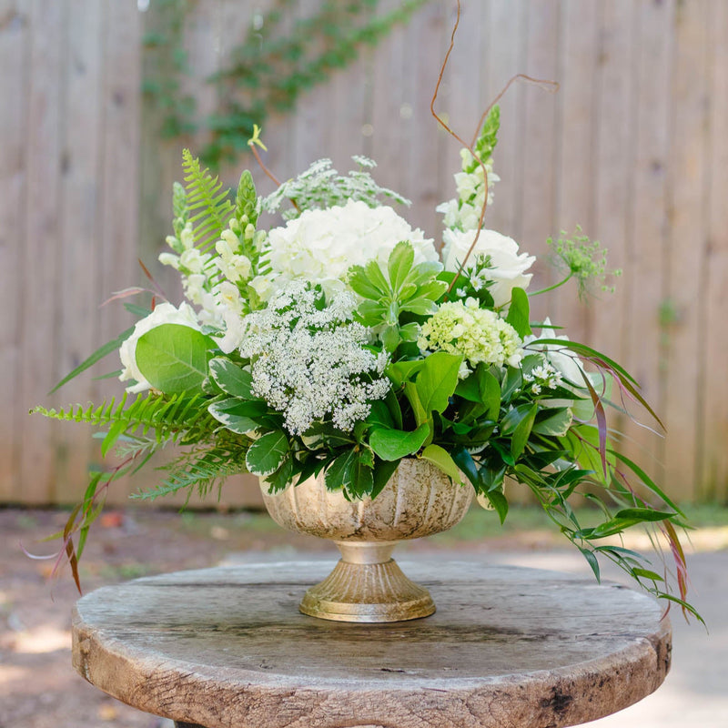 Floral arrangement in a decorative urn on a wooden table with a natural background
