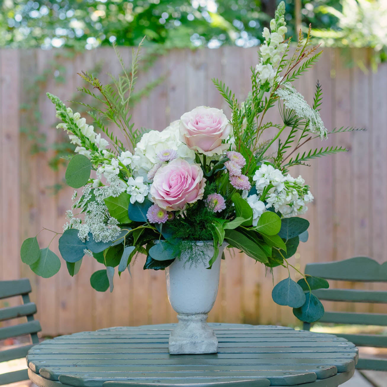 Floral arrangement in a white vase on a green table outdoors.
