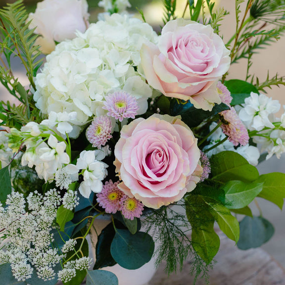 Floral arrangement with pink and white flowers in a white vase on a wooden surface
