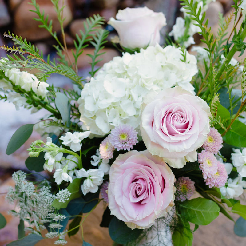 Bouquet of pink and white roses with greenery in a rustic setting.
