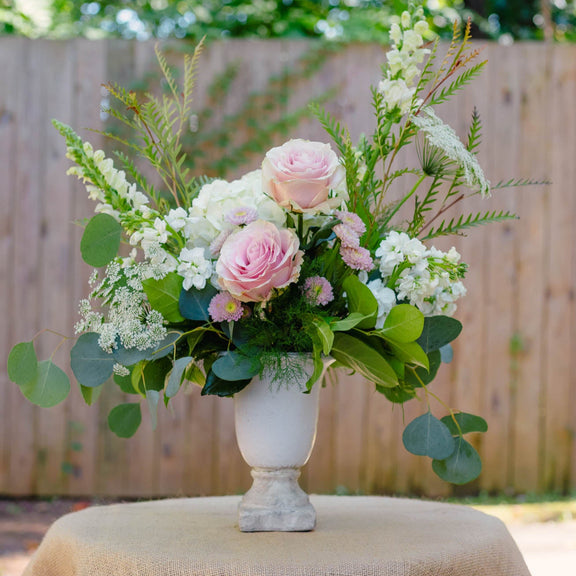 Floral arrangement in a white vase on a table with a burlap tablecloth, outdoors.