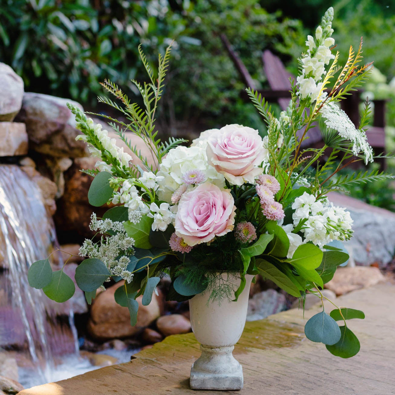 Floral arrangement in a vase with a waterfall and greenery in the background