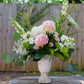 Floral arrangement in a white vase on a wooden table with a blurred green outdoor background