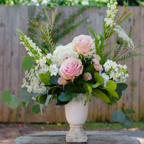 Floral arrangement in a white vase on a wooden table with a blurred green outdoor background