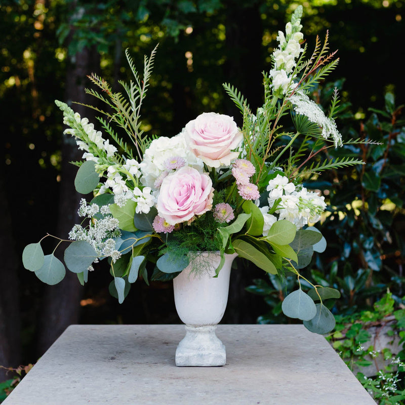 Floral arrangement in a white vase on a stone pedestal with a blurred green foliage background