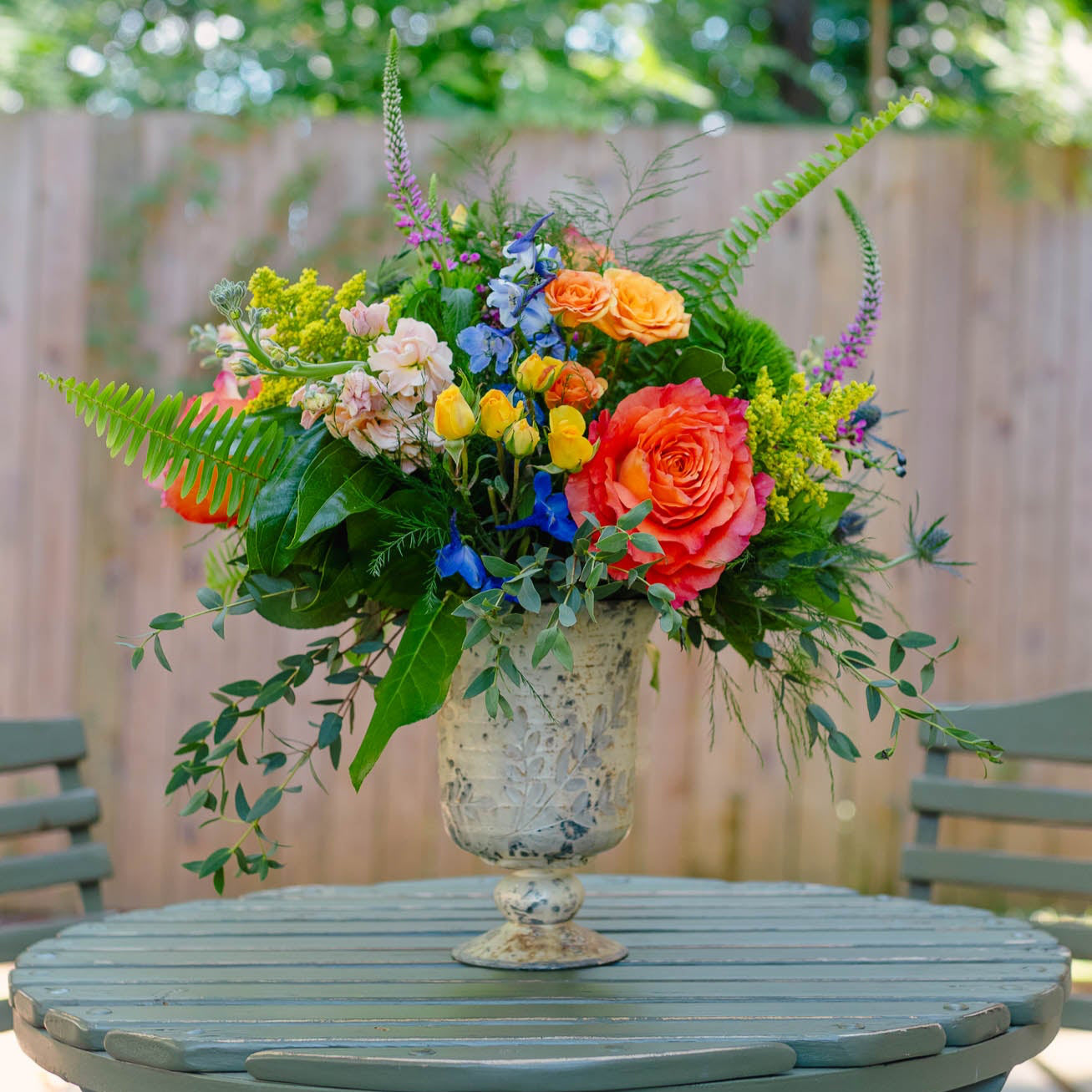 Colorful floral arrangement in a vase on a wooden table outdoors.