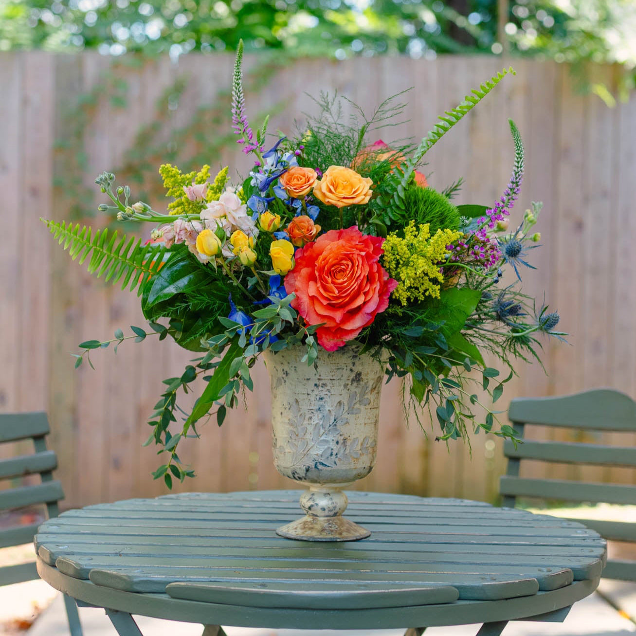 Colorful flower arrangement in a vase on a round wooden table outdoors.