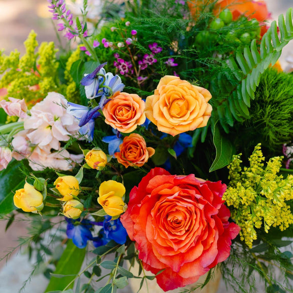 Colorful flower arrangement with roses and other flowers in a glass vase on a wooden surface.