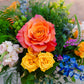 Bouquet of colorful flowers including orange, yellow, and blue roses with greenery.