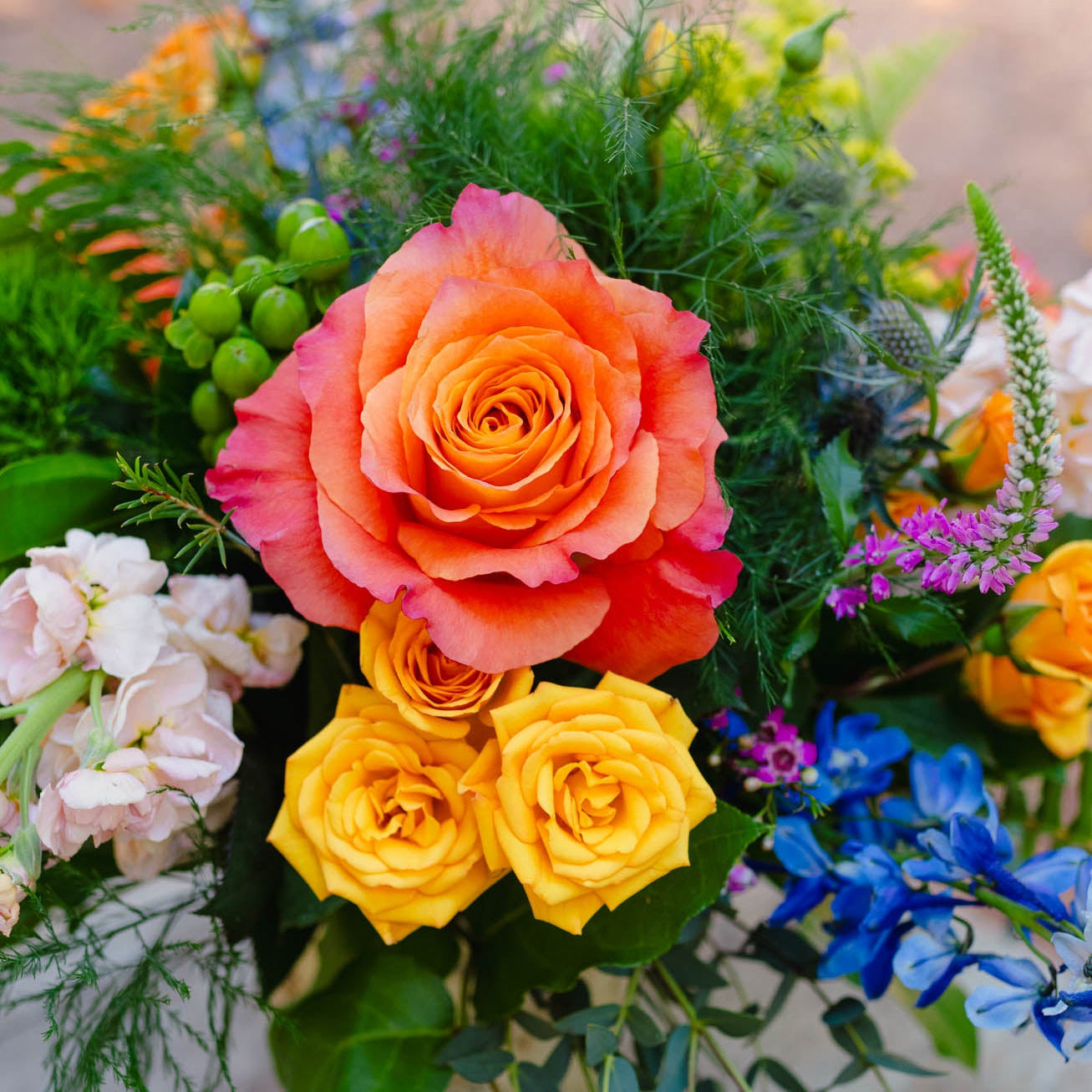 Bouquet of colorful flowers including orange, yellow, and blue roses with greenery.
